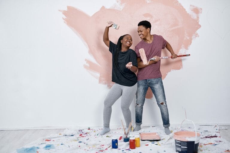 Photo of a man and woman painting a wall pink.
