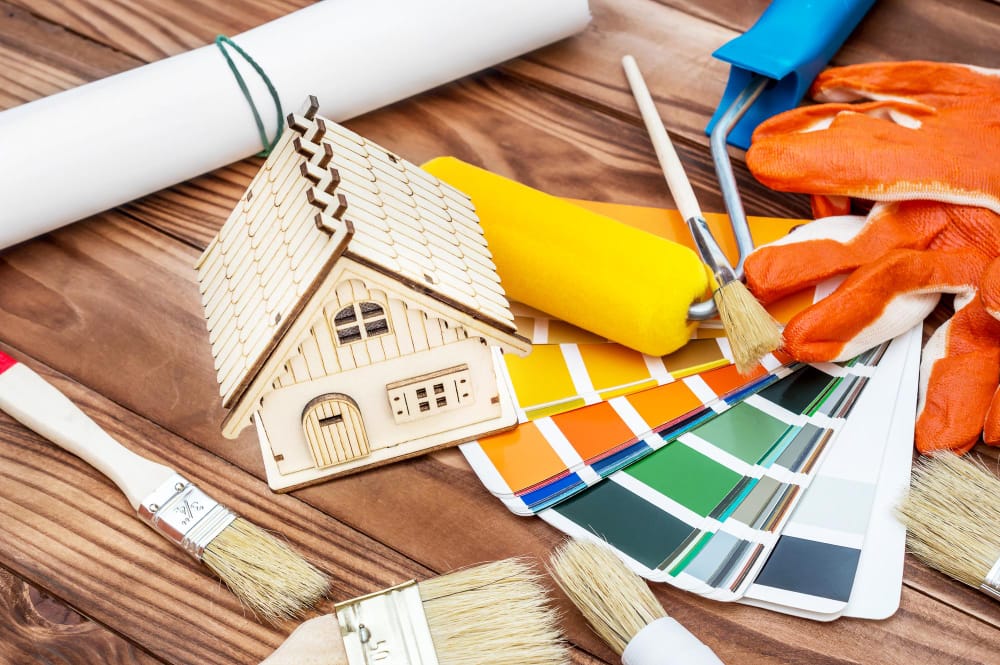 Photo of paint colors, a small wooden house and paintbrushes.